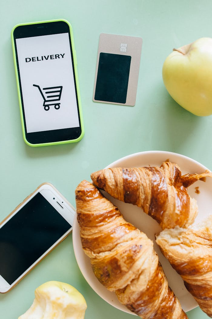 Flat lay of croissants, smartphones, and an apple showcasing a delivery concept.